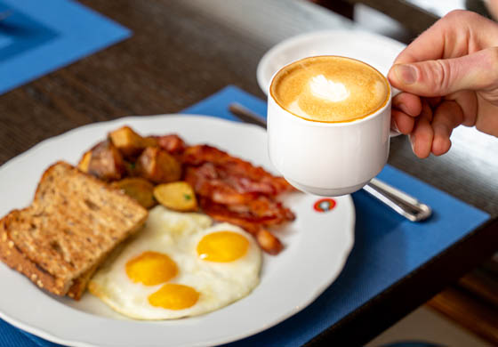 Sunny side up eggs, bacon, and toast on a plate in front of a guest who's drinking a coffee in the Oak Room